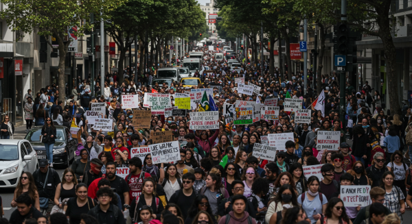 Large crowd of protesters holding placards and chanting slogans in a busy city street, captured in daylight #3