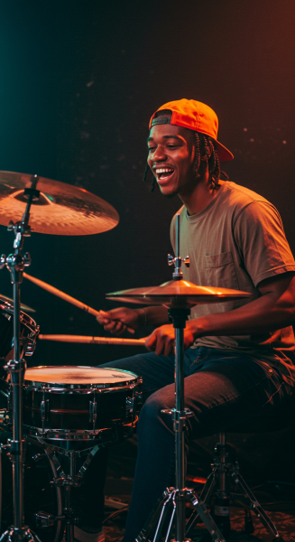 A young black man playing drums and smiling with a cap #2