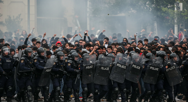 Police officers in riot gear forming a barricade against an angry crowd, smoke in the background #1