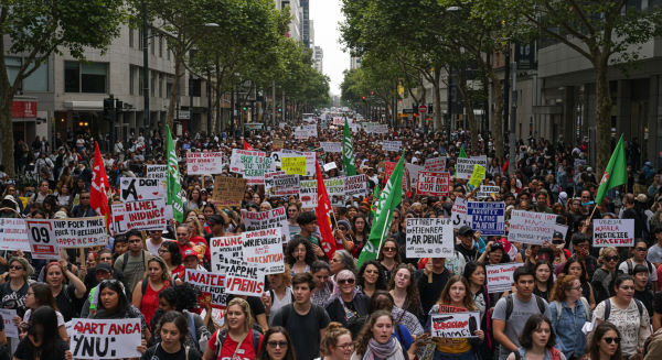Large crowd of protesters holding placards and chanting slogans in a busy city street, captured in daylight #1