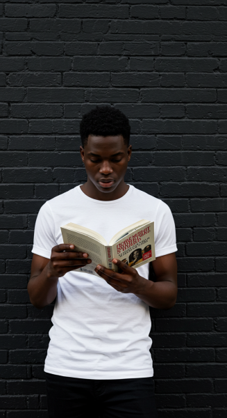 A young black man reading a book while standing by a black brick wall #4