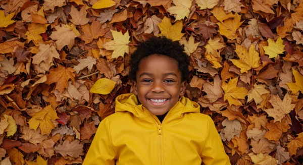 Overhead shot of a black kid smiling in yellow rain jacket and lying in a pile of fall leaves #2