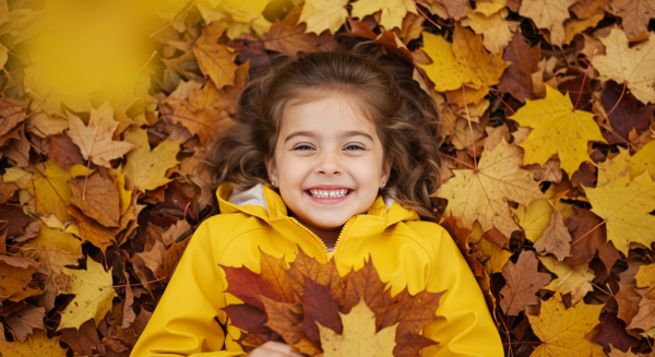 Overhead shot of a kid smiling in yellow rain jacket and lying in a pile of fall leaves #2