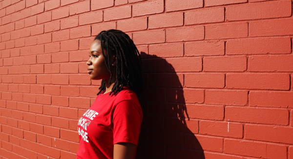 A young black woman in a red shirt standing by a red wall in a far-off shot #4