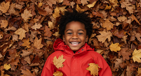 Overhead shot of a black kid smiling in red rain jacket and lying in a pile of fall leaves #4