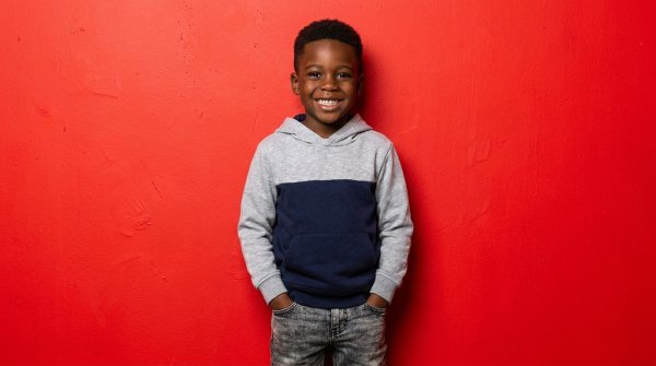Happy black boy in casual hoodie posing in front of a vibrant red backdrop