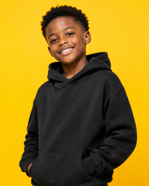 Happy black boy in casual hoodie posing in front of a vibrant yellow backdrop