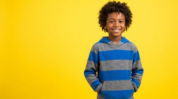 Happy black boy in casual hoodie posing in front of a vibrant yellow backdrop