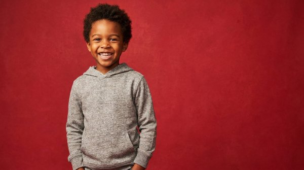 Happy black boy in casual hoodie posing in front of a vibrant red backdrop